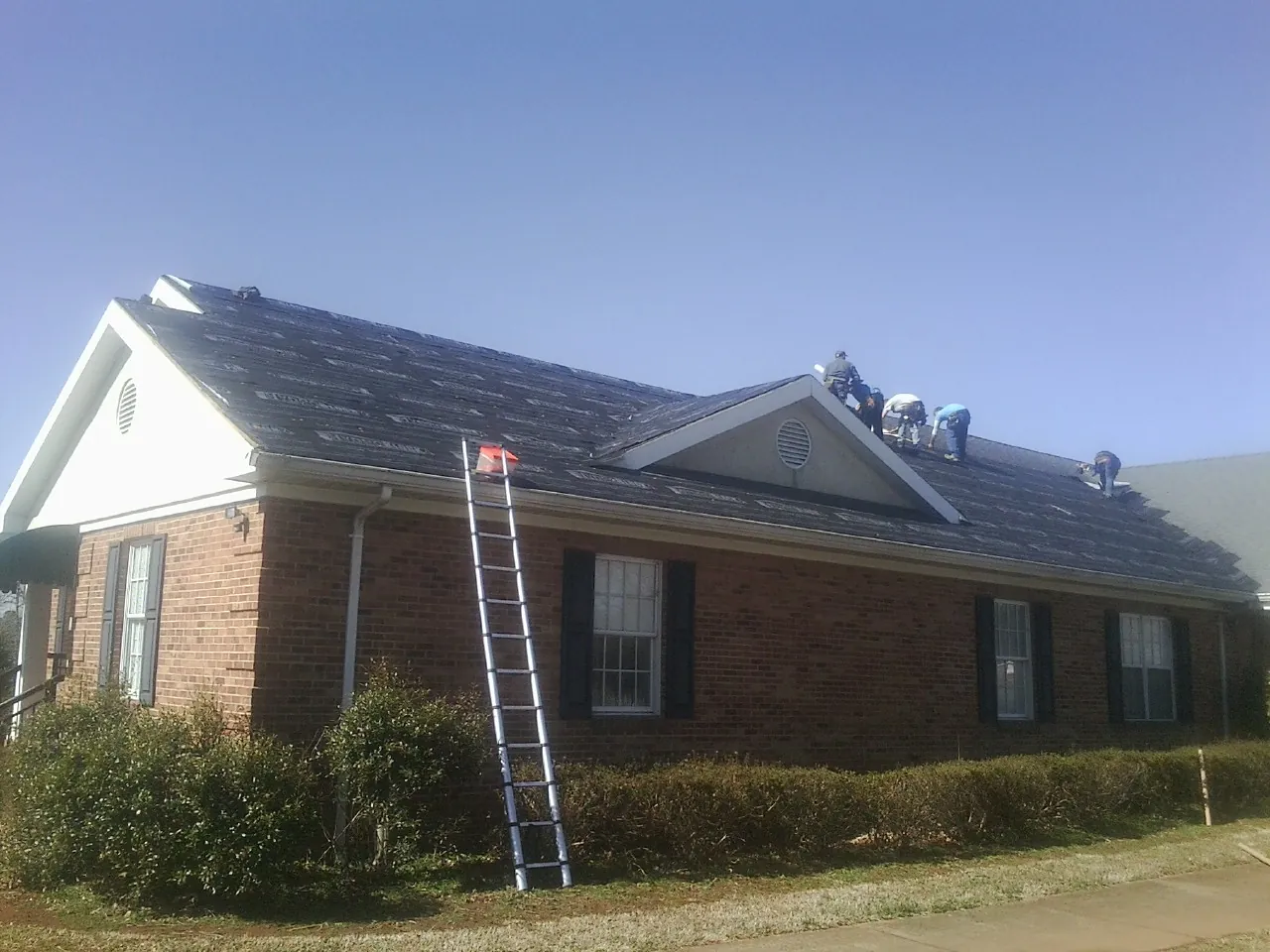 Crew tearing shingles off a brick ranch roof with a ladder set — Metal Roof Repair work by our crew in North Manchester