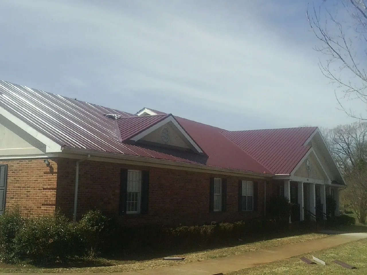 Red metal roof with gabled entries on a long brick building, from a Hail Damage Roof Repair job in North Manchester