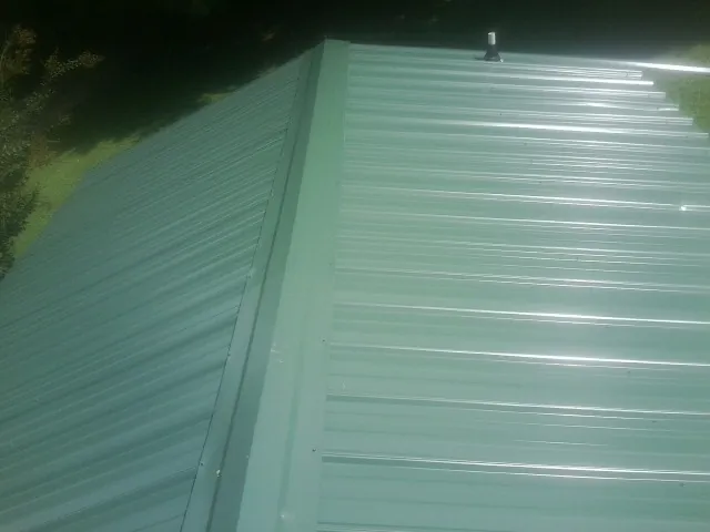 New green metal panels meeting at the ridge of a roof — Flat Roof Repair work by our crew in North Manchester