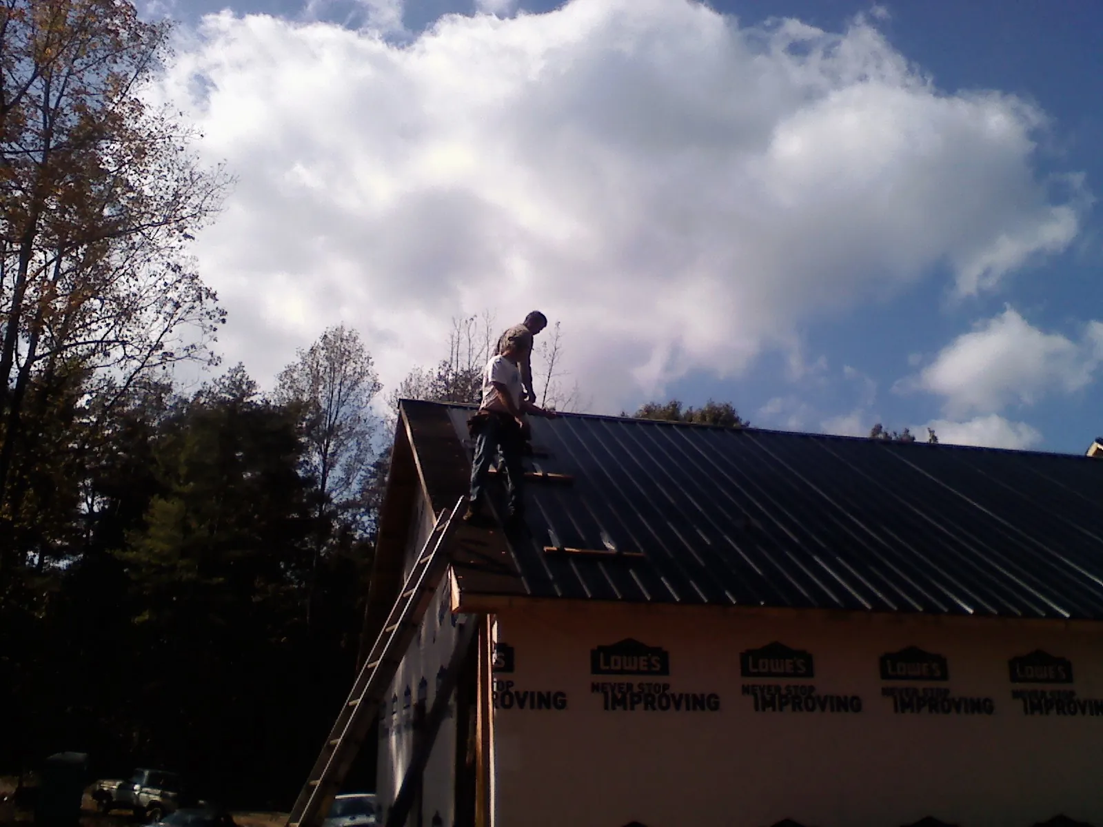 Roofer fastening dark metal panels high against a cloudy sky, from a Roof Inspection job in North Manchester