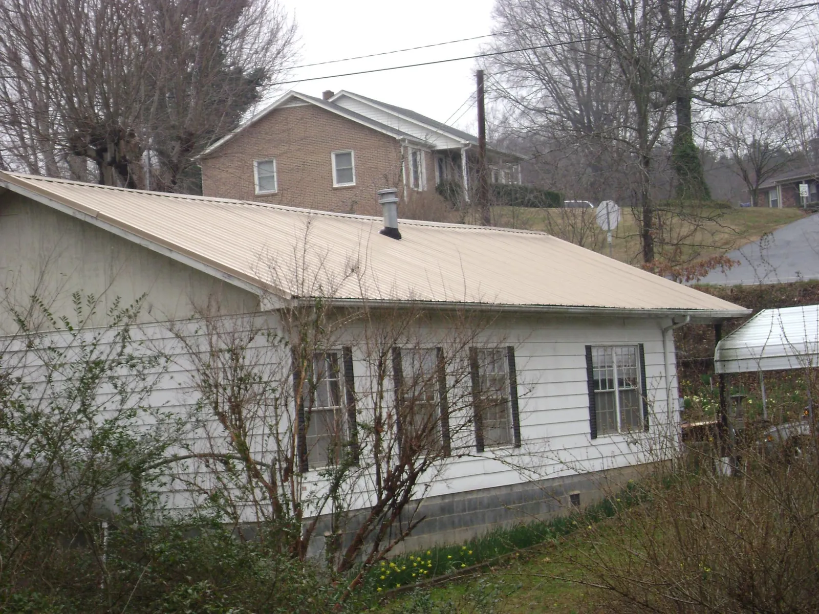 Tan metal roof on a white sided house set into a hillside — Commercial Roofing by Roofing Brothers in North Manchester